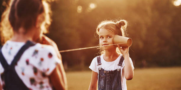 Two female kids stands in the field and talking by using string can phone.