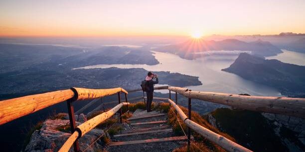 Man photographing landscape with lake and mountains at beautiful sunrise. View from Mount Pilatus, Lucerne, Switzerland